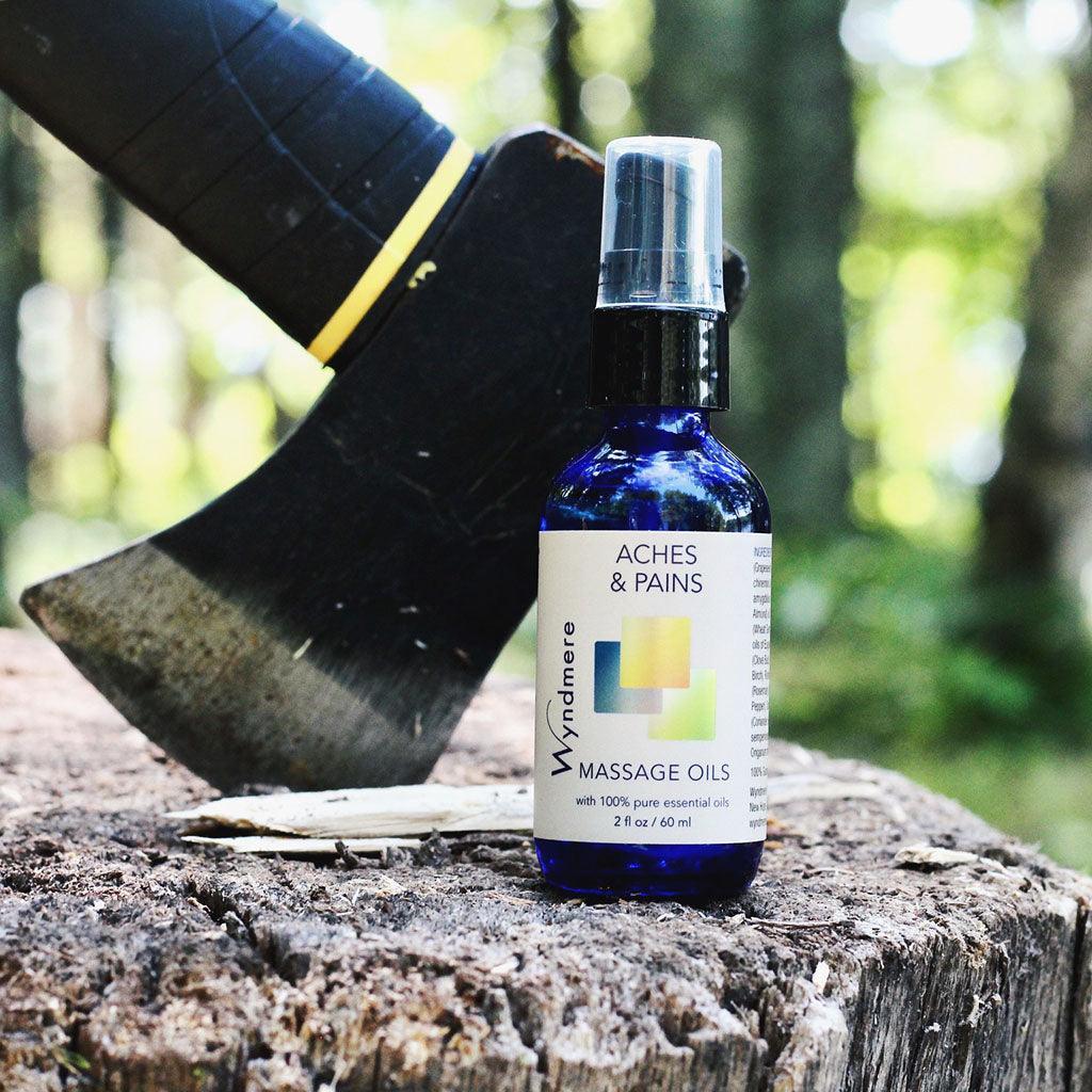 2oz cobalt blue bottle of Aches &amp; Pains Massage Oil on tree stump with ax.