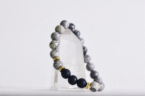 gray beaded aromatherapy bracelet with black lava stones draped on quartz stone