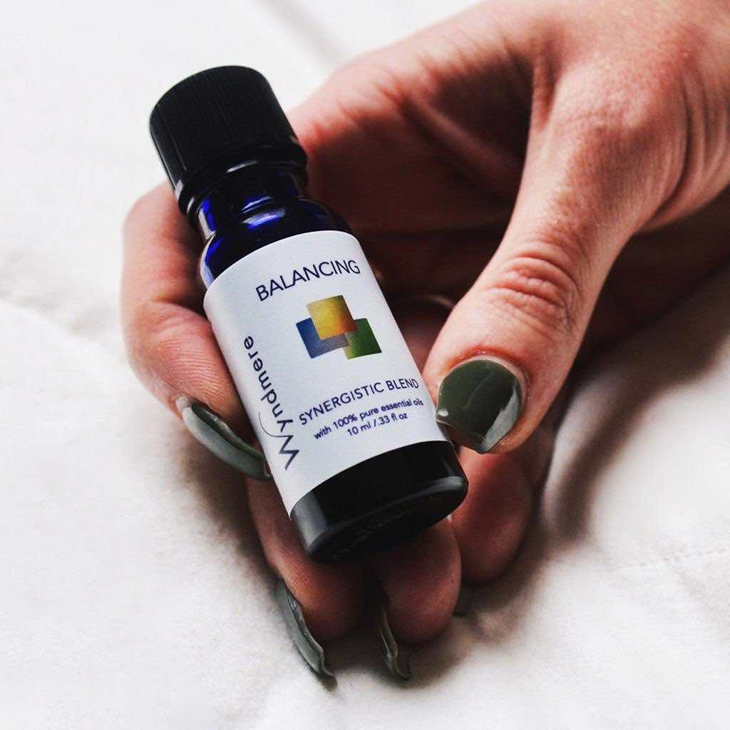 Female hand holding Wyndmere Balancing Essential Oil Blend in a 10ml cobalt blue bottle.