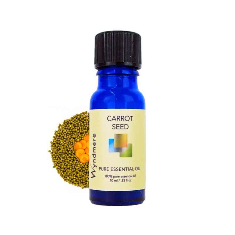 Slices of carrot and seeds with a 10ml cobalt blue bottle of Wyndmere Carrot Seed Essential Oil