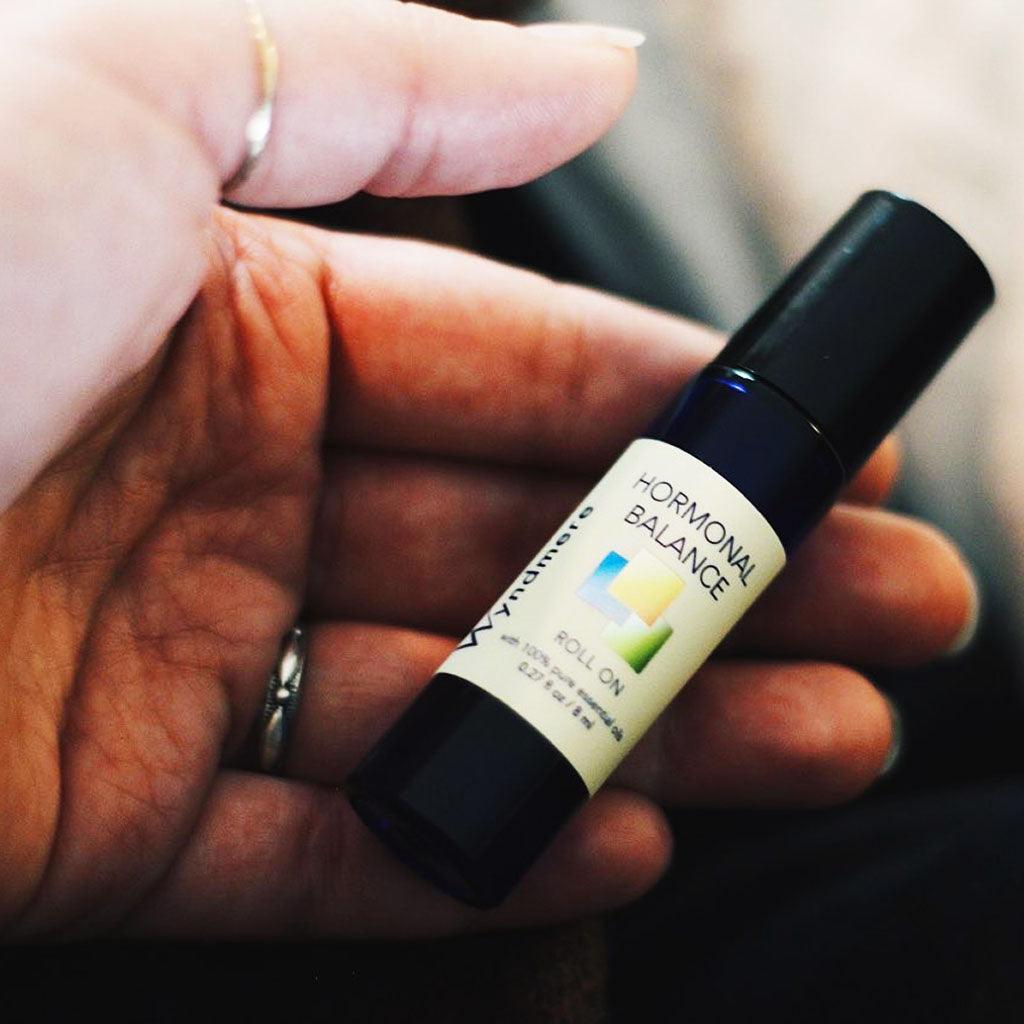 A woman's hand craddling a cobalt blue bottle of Hormonal Balance roll-on.