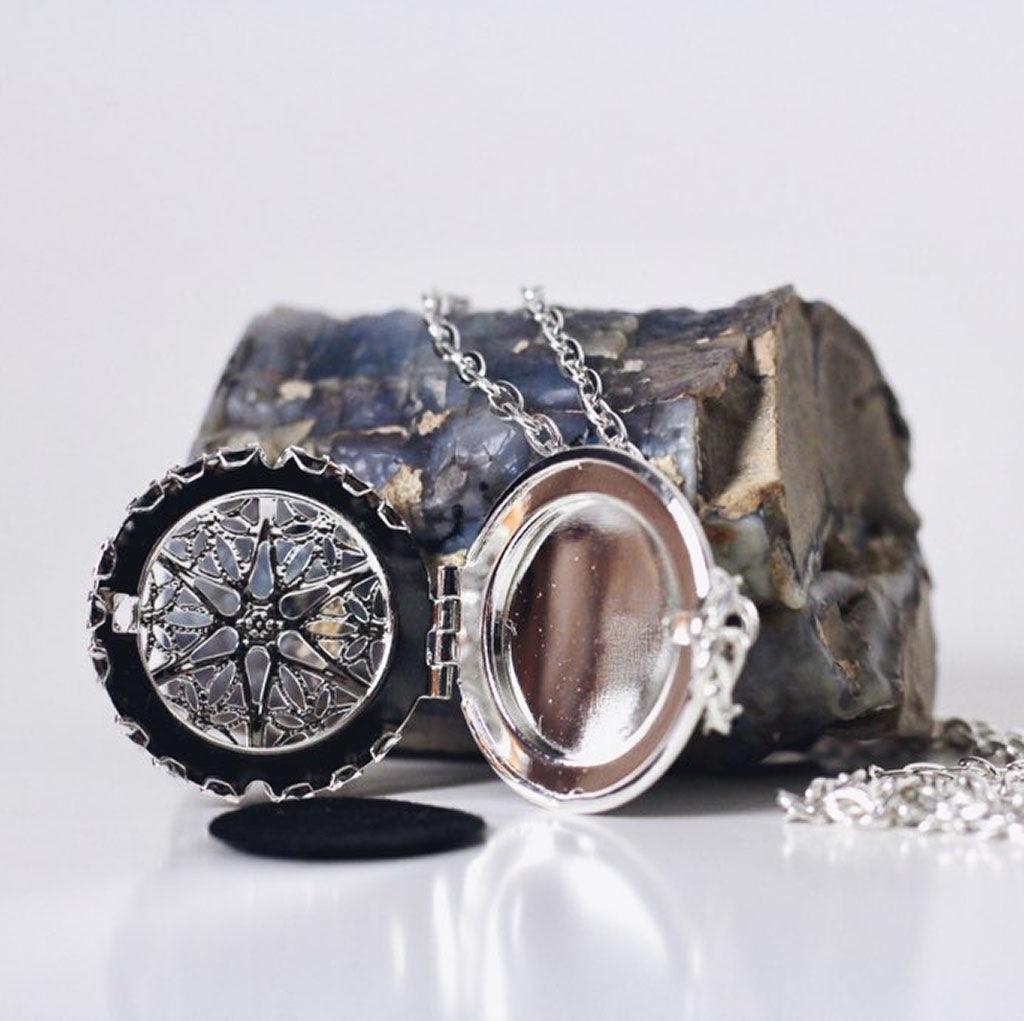 aromatherapy necklace leaning against rock with the silver pendant open and a fragrance pad laying near