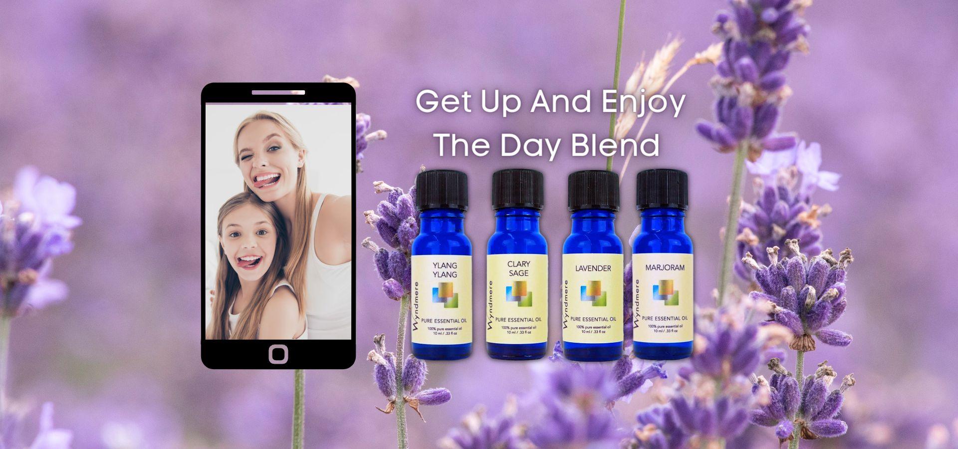 Wyndmere Naturals - Wake up and enjoy the day blend. Picture of mother and daughter taking a selfie being silly on a iphone frame. With lavender flower background. Bottles of lavender, ylang ylang, marjoram, clary sage essential oils. 