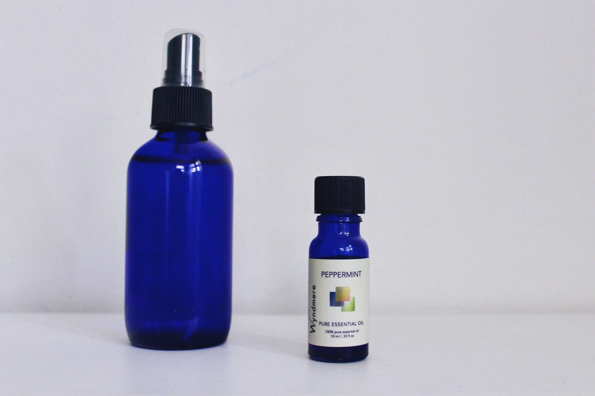 Empty cobalt blue spray bottle with bottle of peppermint essential oil