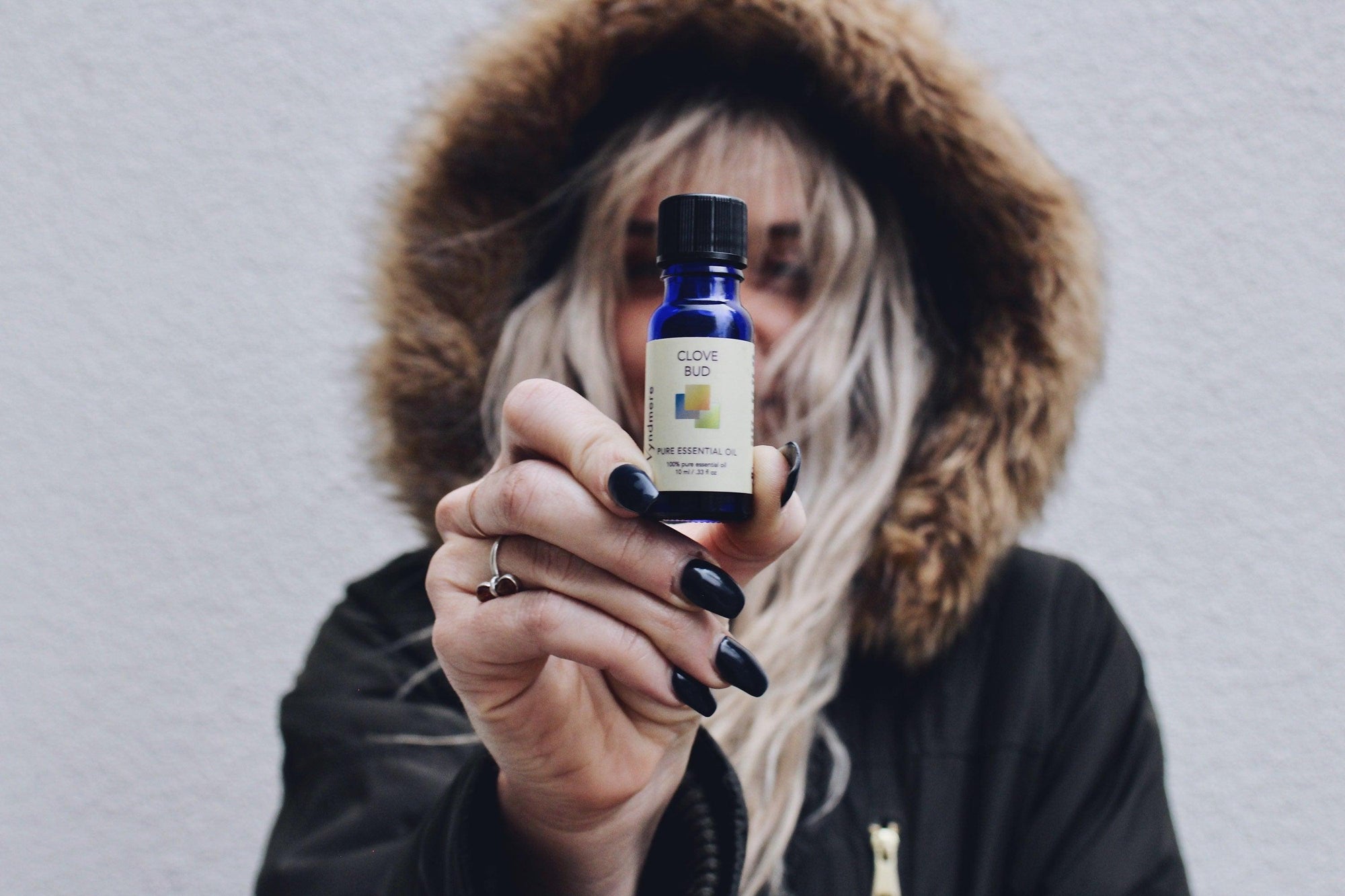 Woman with hooded coat holding a bottle of Wyndmere clove bud essential oil