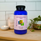 Blue bottle of Wyndmere Detoxification Aide Bath Salt on a wooden surface with a white tiled wall background.