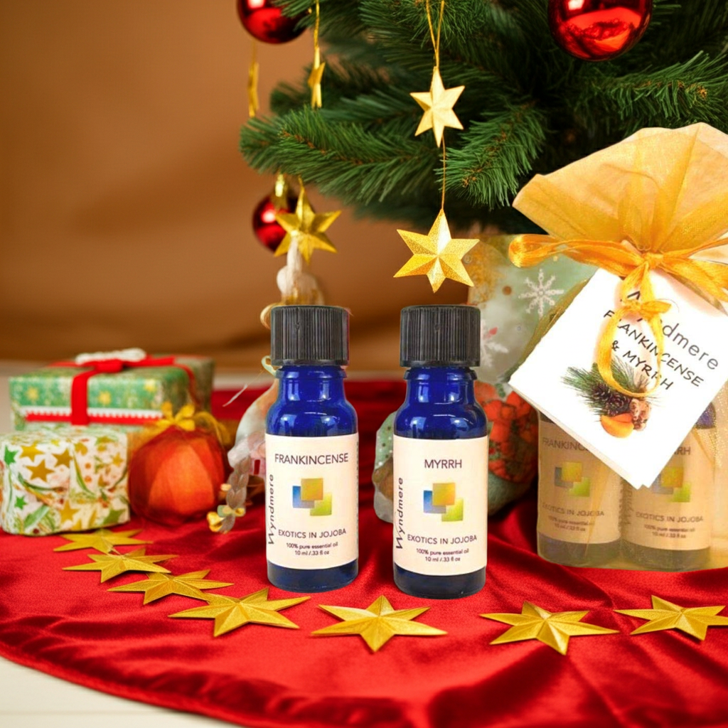 Two bottles of Wyndmere Frankincense and Myrrh essential oil on a red surface with Christmas decorations in the background.