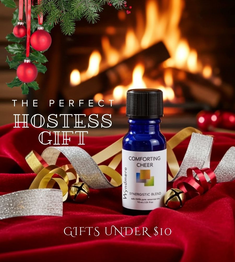 Bottle of 'Wyndmere Comforting Cheer' essential oil blend on a red surface with festive decorations and a fireplace in the background.