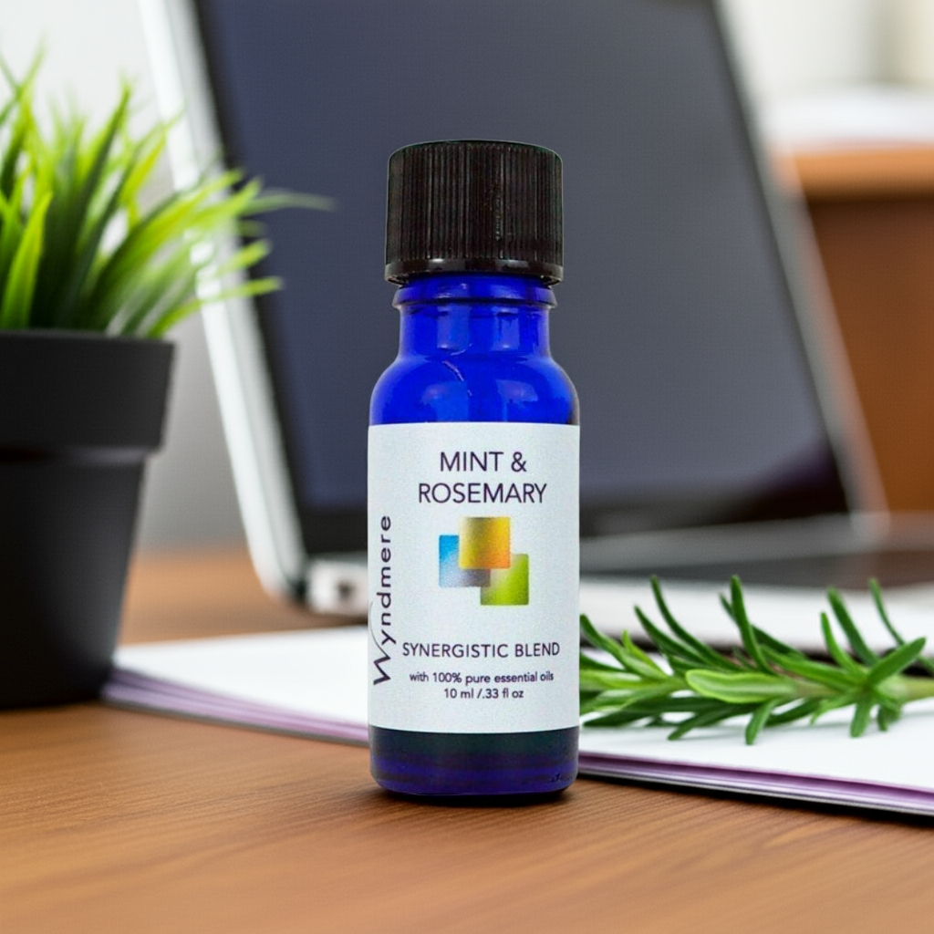 Bottle of Wyndmere Mint &amp; Rosemary essential oil blend on a desk with a laptop and plant in the background