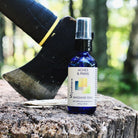 2oz cobalt blue bottle of Aches & Pains Massage Oil on tree stump with ax.