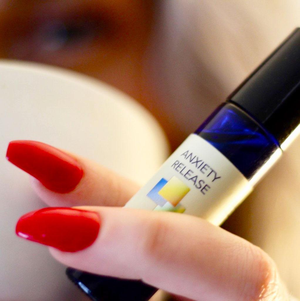 Woman with red fingernails holding roll on bottle of Anxiety Release and cup of tea.