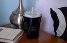 Black AromaSens ultrasonic diffuser on nightstand with books and lamp base