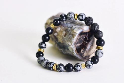 black and charcoal gray beaded aromatherapy bracelet with black lava stones laying on mottled quartz stone