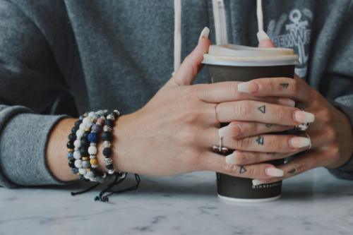 woman wearing 5 aromatherapy bracelets on wrist while cradling a cup of coffee