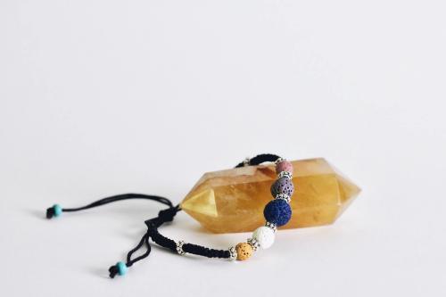 adjustable black corded aromatherapy bracelet with colorful lava beads draped on yellow quartz rock