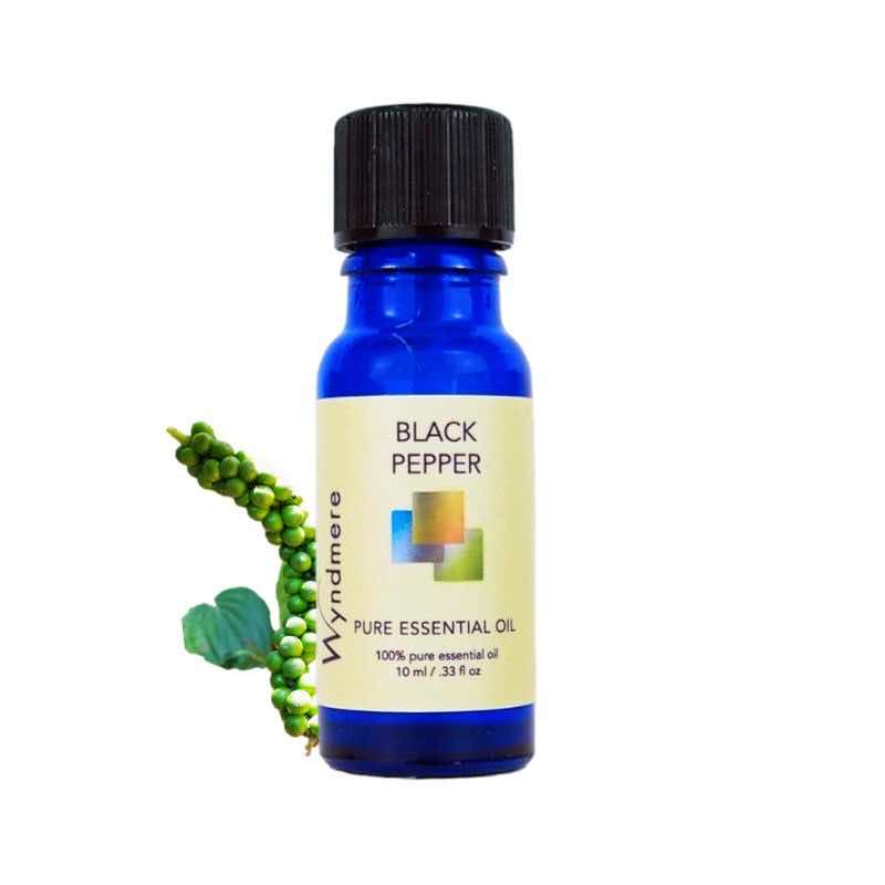Peppercorns and leaf of Black Pepper with a 10ml cobalt blue bottle of Wyndmere Black Pepper Essential Oil