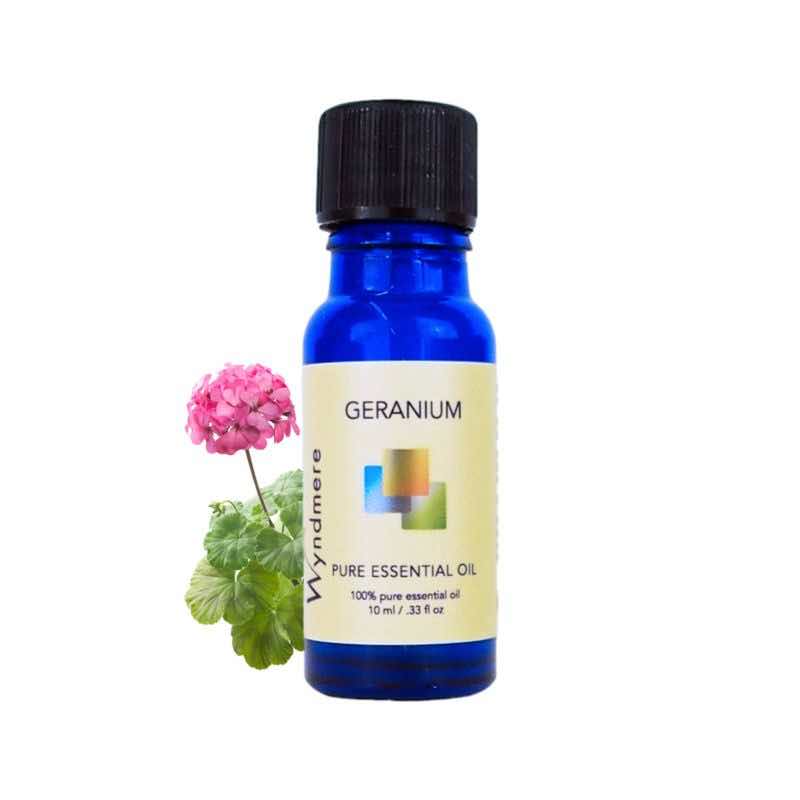 Flower and leaves of Geranium with a 10ml cobalt blue bottle of Wyndmere Geranium Essential Oil