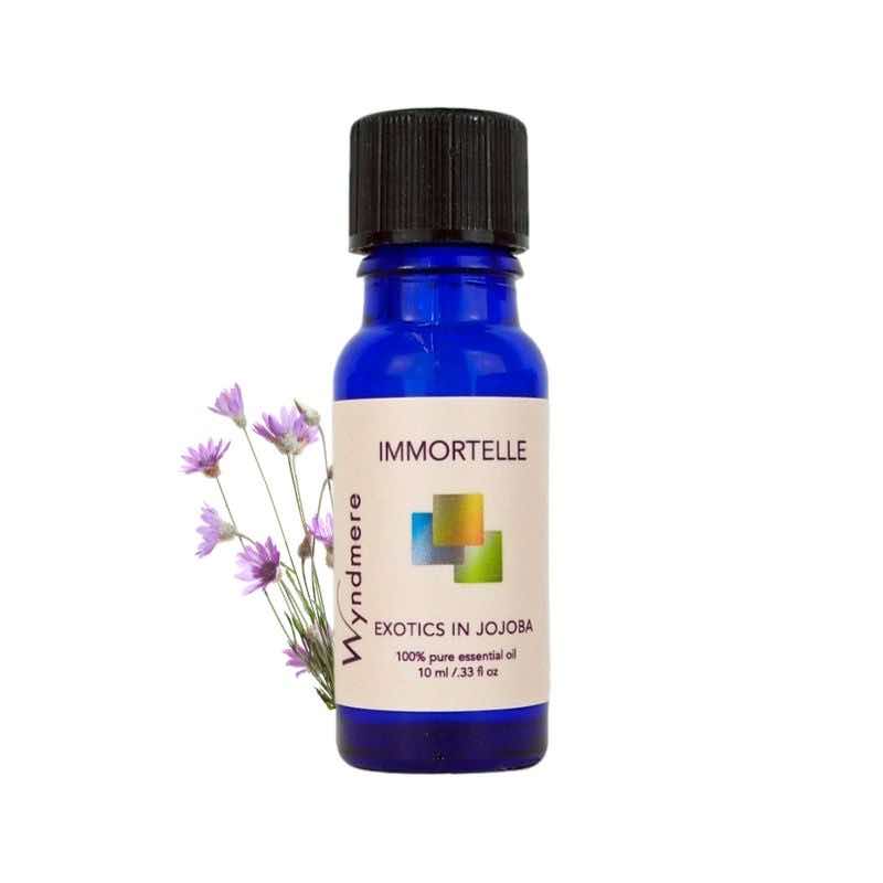 Immortelle flowers with a 10ml blue bottle of Wyndmere Immortelle Essential Oil diluted in Jojoba. Also known as Helichrysum