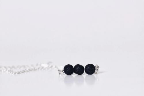 aromatherapy necklace of 3 black lava beads on a silver chain laying on white counter