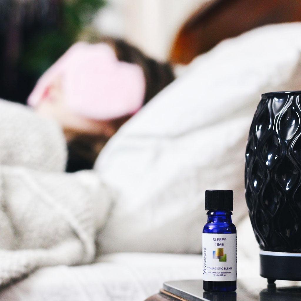 Bottle of Sleepy Time essential oil blend and aroma vase diffuser with sleeping woman in background